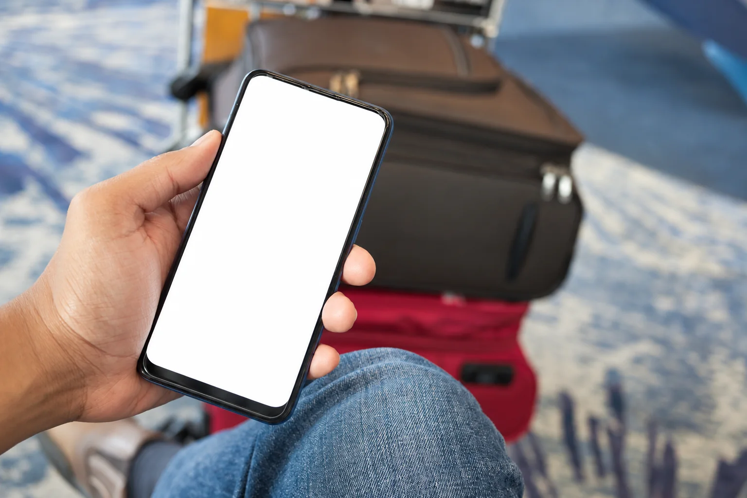 A traveler holding a phone with a blank screen beside luggage.