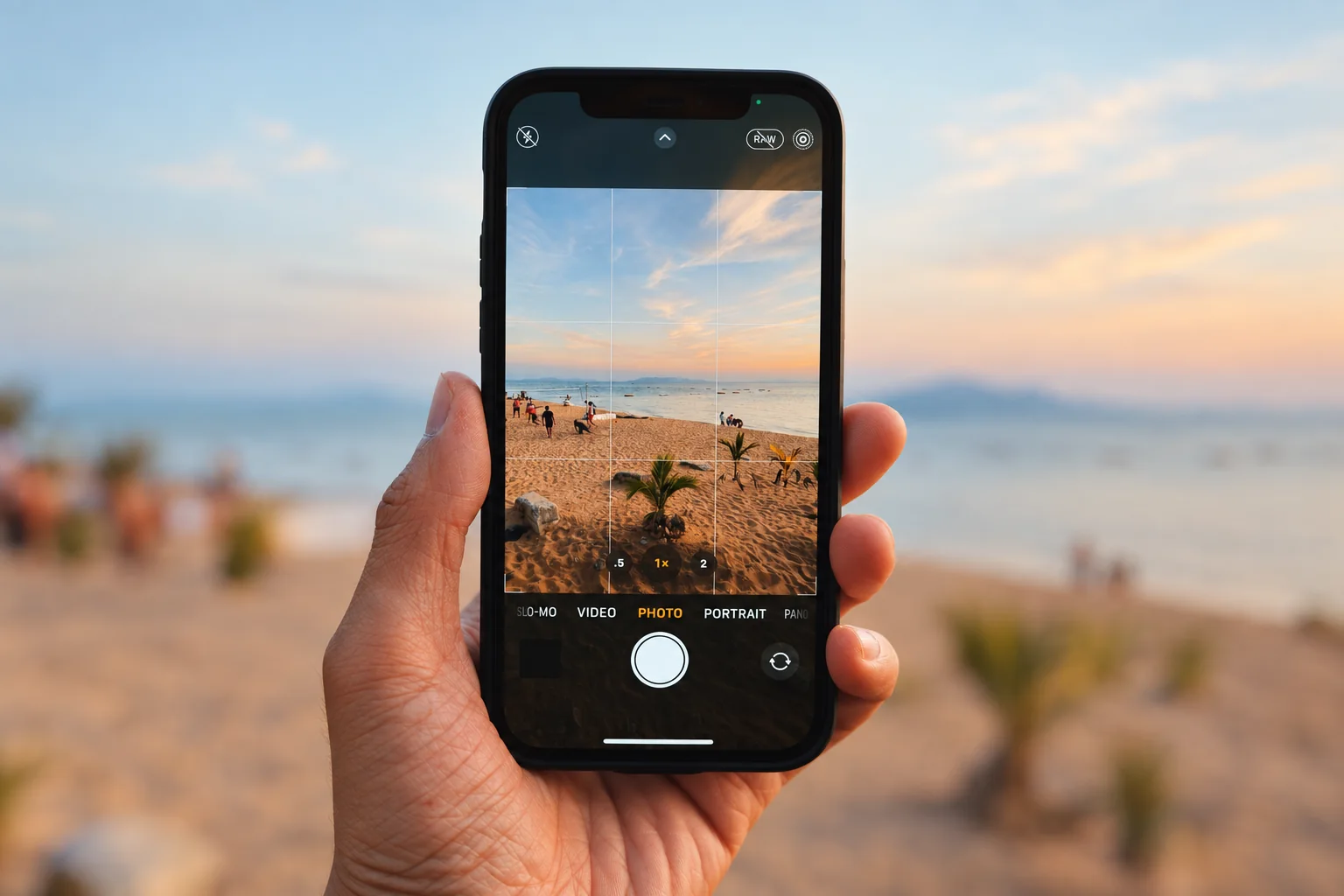 A hand holding a phone while photographing a beach.