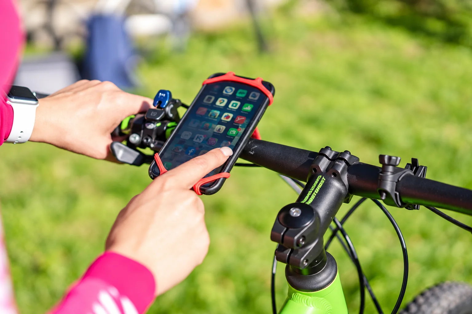 A phone secured to bicycle handlebars by a red elastic mount.