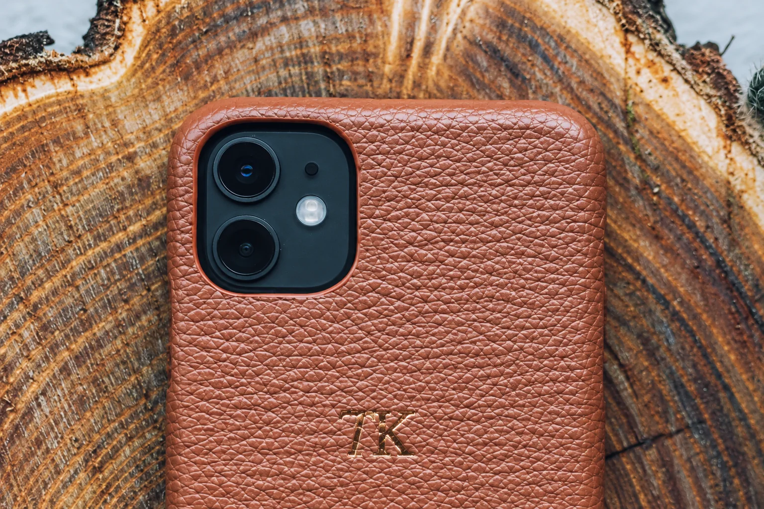 A brown textured phone case resting on a tree cross section.