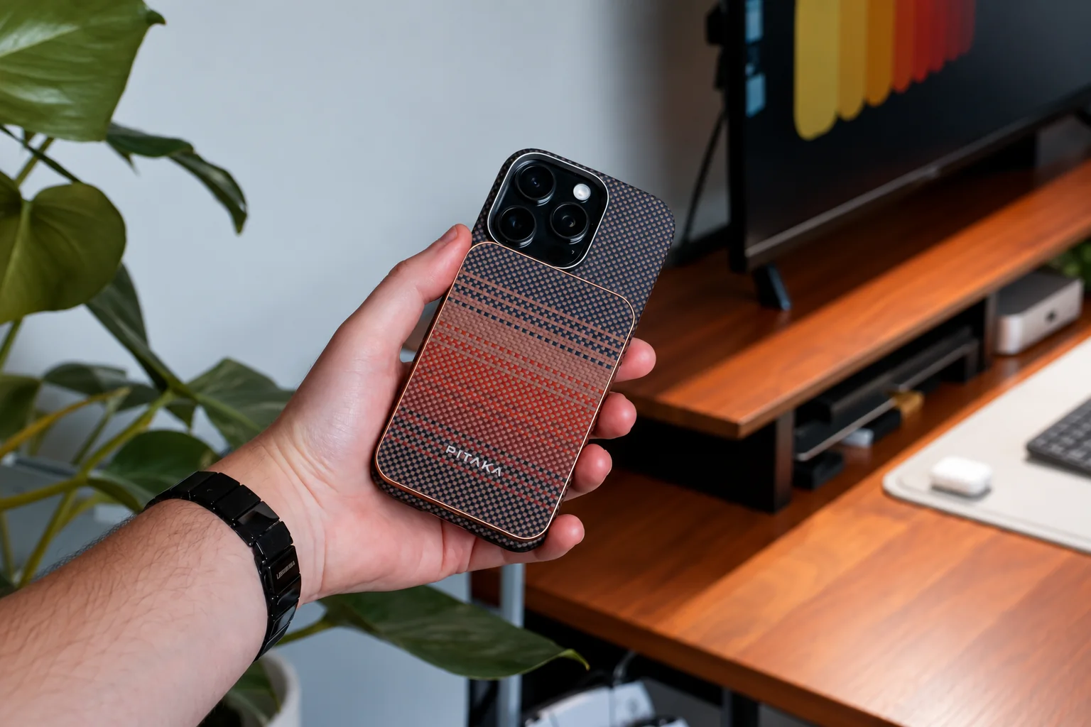 A hand holding a phone with a patterned PITAKA magnetic battery pack.