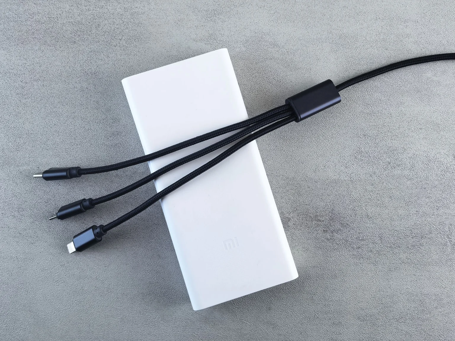 A white power bank beside a separate cable with three connectors.
