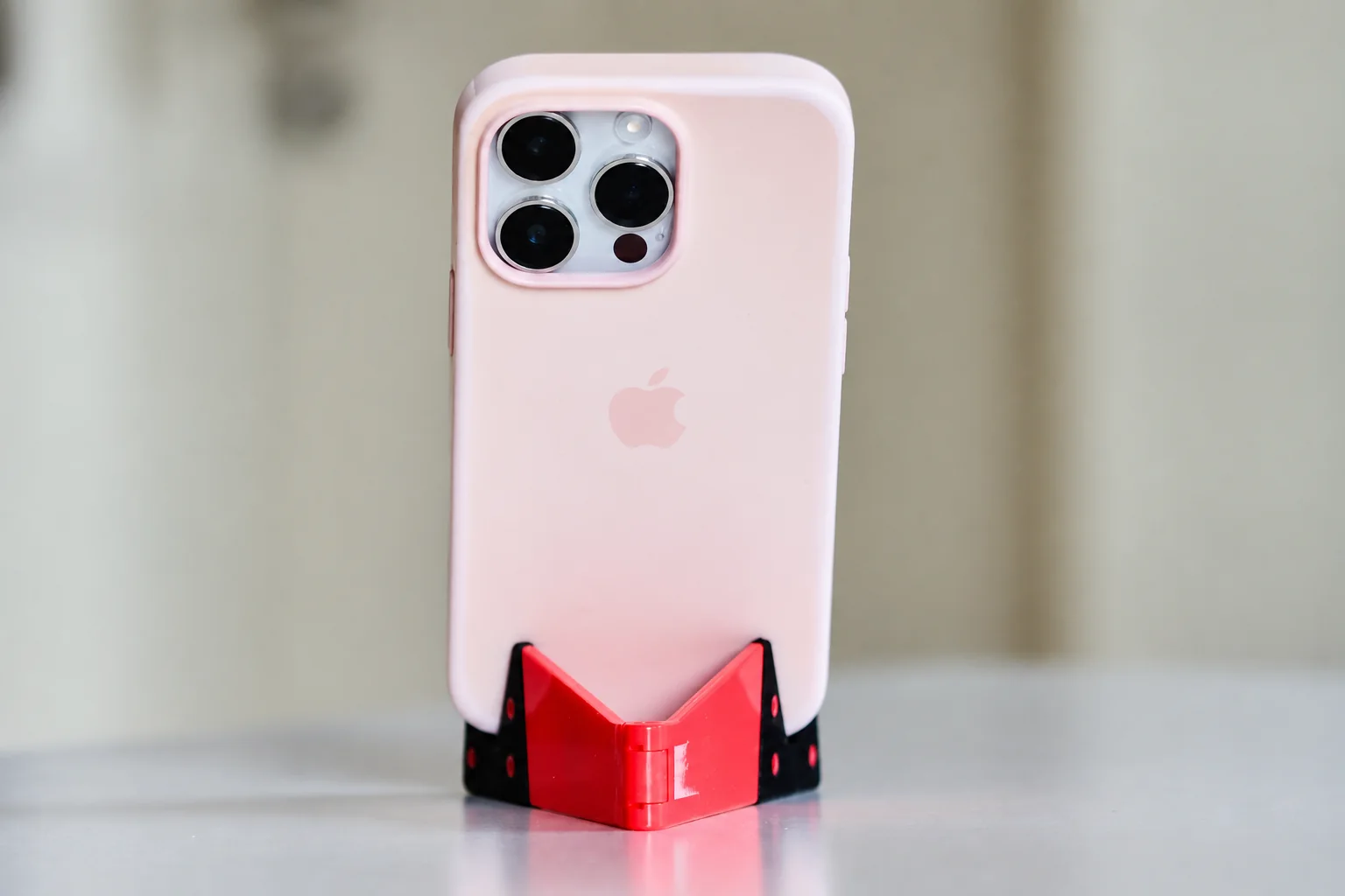 A phone in a pale pink case resting in a red folding stand.