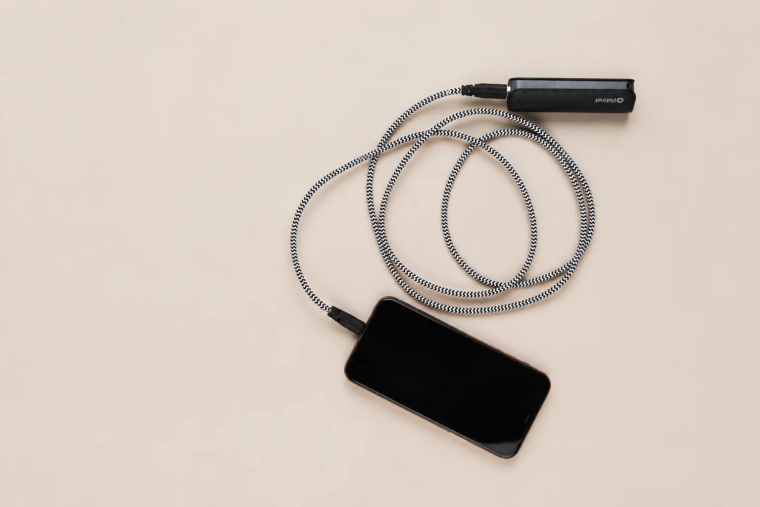 A small power bank connected to a phone by a coiled braided cable.