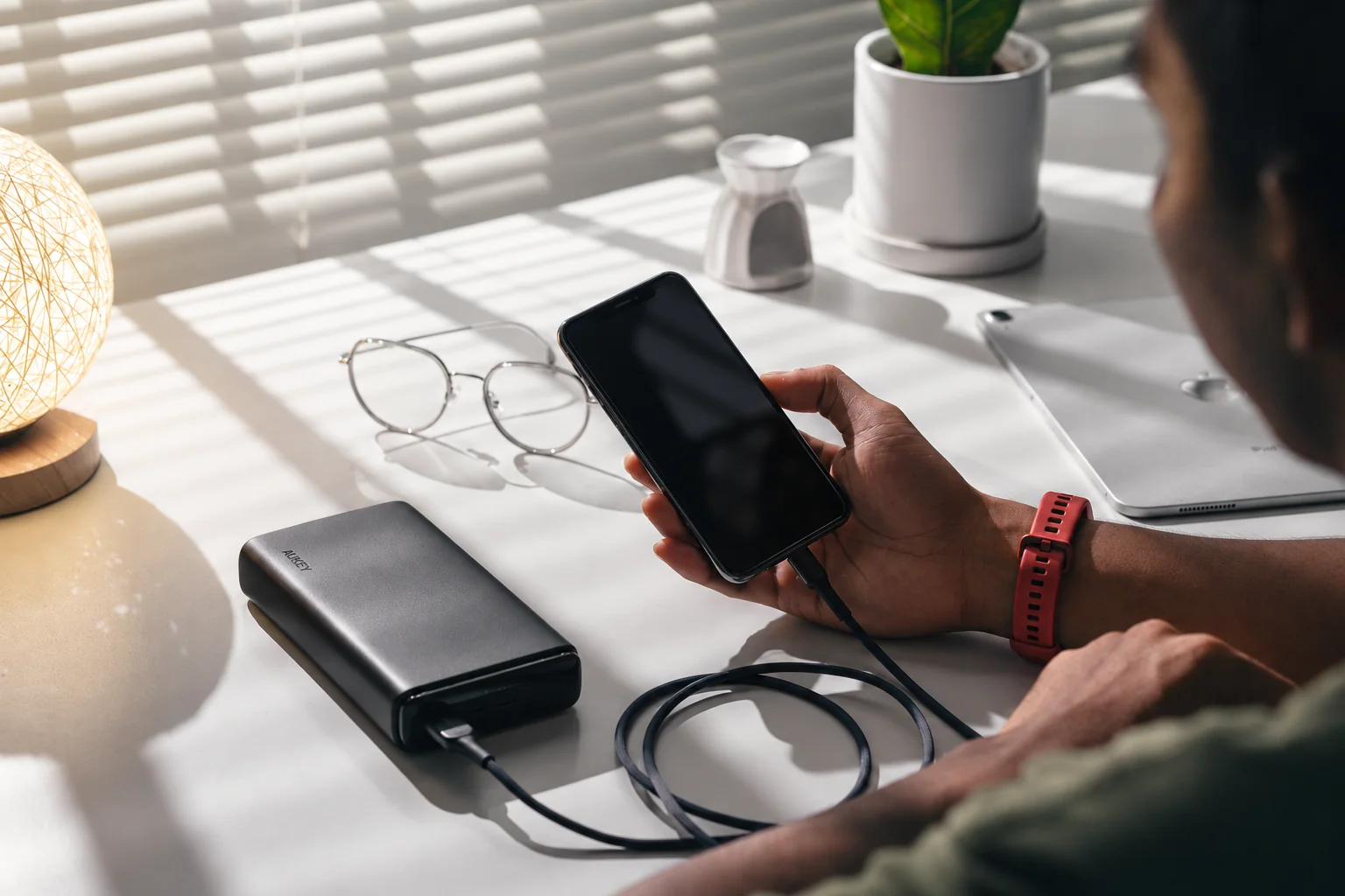 A person holding a phone connected to an AUKEY power bank on a desk.