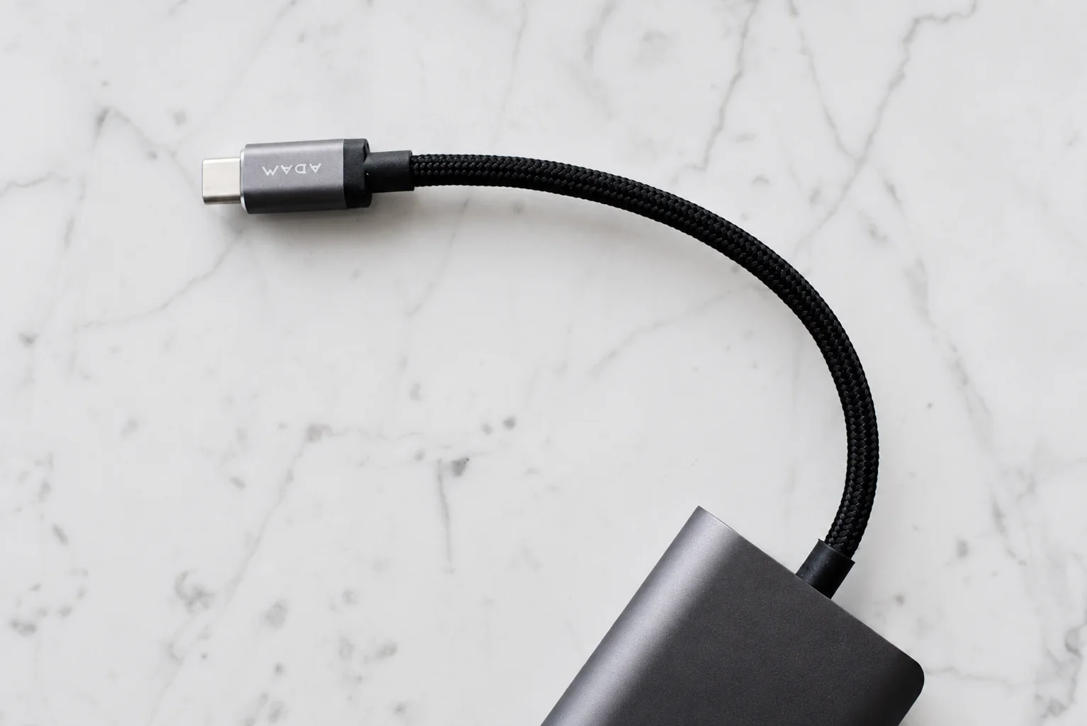 A braided USB-C lead attached to a grey hub on a marble surface.
