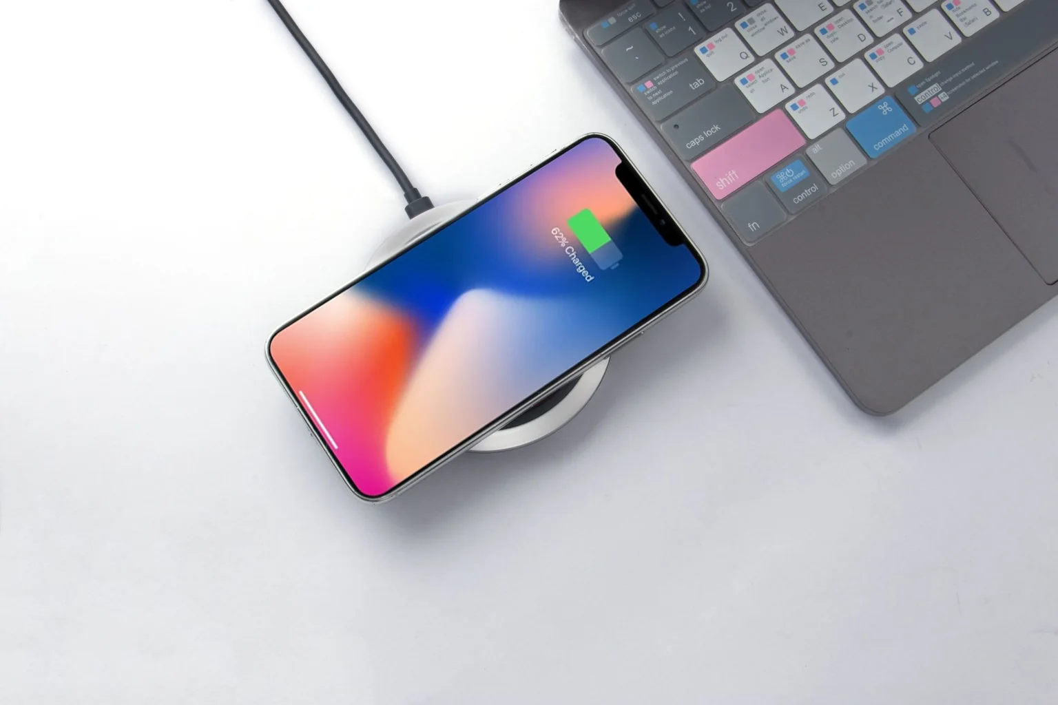 A phone on a wireless charging pad beside a laptop keyboard.